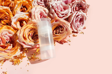 Unbranded transparent bottle of Intimate lubricant gel and pink golden roses on pink background with copy space. Intimate massage and comfortable sex consept. Lifestyle, flatlay, top view, template