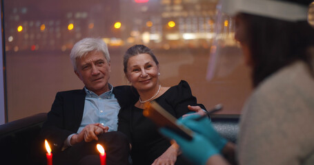 Happy aged couple with menu ordering meal in restaurant