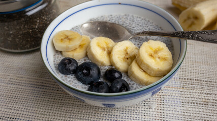 Chia seed pudding with almond milk, banana and blueberries in a decorated blue and white bowl and a silver spoon for breakfast. Close up.