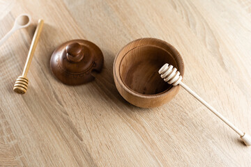 Honey with wooden honey dipper in wooden bowl on wooden table