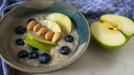 Bowl of oatmeal with nuts, almonds, granny smith green apples, blueberries on table. Top view of organic porridge  in a ceramic rustic bowl.