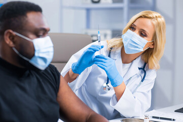 Professional doctor makes a coronavirus vaccine using a syringe and hypodermic needle. Professional medical worker and patient at the hospital office. Vaccination and safety.