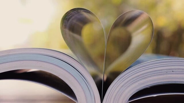 close-up of heart shape from book for love on wood table with blurred nature background in wind blowing with sunlight shining, zoom out shots