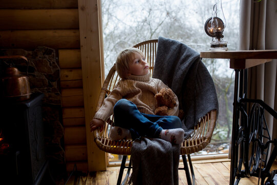 Cute toddler child in a little fancy wooden cottage, reading a book, drinking tea