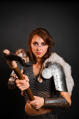 Woman warrior in chain mail armor with lamellar bracers and plate shoulder pad with the fur of a polar fox on her shoulders, stands in a fighting stance with an ax in her hands against dark background