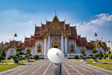 Marble buddhist temple with beautiful Thai lady standing in front holding an umbrella. 