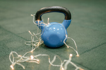 Kettle bells in a Gym. Christmas fitness composition with blue dumbbells, gift on white background with bokeh and show. Greeting card for fitness club with copy space.