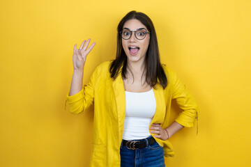 Young brunette businesswoman wearing yellow blazer over yellow background showing and pointing up with fingers number four while smiling confident and happy