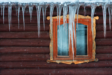 Roof of hous and window in huge hanging icicles. Winter in the countryside. Wooden house outside....