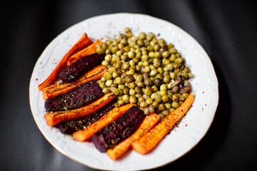 spicy peas and carrots baked in the oven. a delicious vegan meal on black background and blurry view.