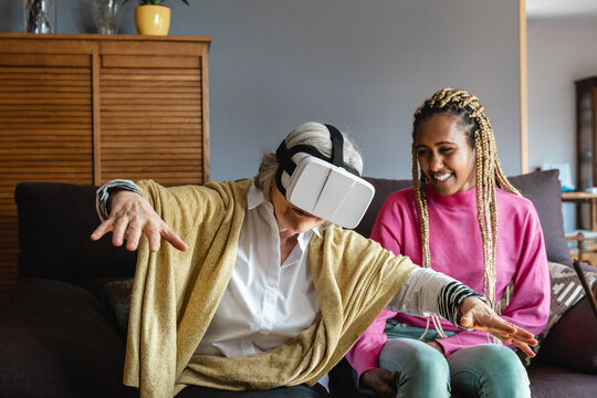 Multiracial senior and young woman playing console games wearing vr headset at home - Focus on googles