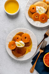 Delicious pancakes with tangerines and honey or maple syrup for breakfast on a light background.