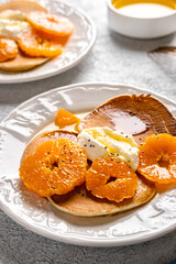 Close-up delicious pancakes with tangerines and honey or maple syrup for breakfast on a light background.