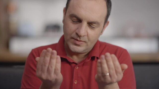 Young Muslim man at home with open palms praying to God.Praying man.Slow motion video.Close up.