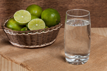 Glass with water and basket with lemons to prepare a drink.
