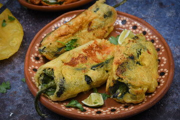 Mexican chiles rellenos stuffed with potato and cheese, vegan batter, served in traditional clay dish