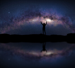 Naklejka na ściany i meble Female silhouette raises arms in front of a bright Milky Way night sky. Concept about open air sport activity, adventure, travel.