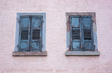 Facade of an old abandoned building with peeling light blue paint on window shades.