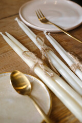 Golden spoon and fork with withe plate are in the wooden table. White fox candles 