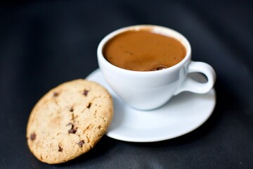 Turkish coffee in a white porcelain glass and chocolate chip cookies. Blurry and black background.