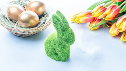 Easter Golden eggs in basket with spring tulips, white feathers on pastel blue background in Happy Easter decoration. Spring holiday concept.