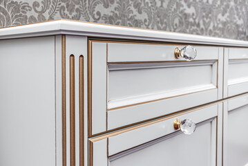 Classical bedside table with drawers and crystal handles on floral wallpaper background, closeup