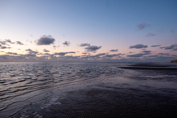 View of the setting sun shining on the Sea and reflected on the beach, clouds with sun-shining edges. Landscape. High quality photo showing concept of freedom and dreams