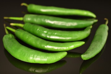 A few dark green organic, natural, spicy, hot pepper pods on a black background.