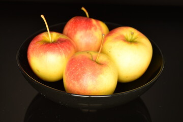 Several fresh organic, juicy, sweet, aromatic apples in a black ceramic plate, on a black background, close-up.