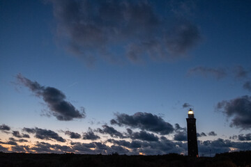 Lighthouse standing on the Dutch coast with a dramatic. and colorful dusk or dawn sky behind it. High quality photo