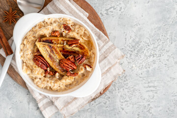 Oatmeal with fried banana, cinnamon, and honey in a white bowl on a gray concrete background top view. Sweet tasty breakfast. Copy space for text.