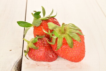 Three diet strawberries, close-up, on a painted wooden table.