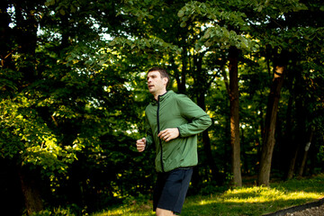 Athletic young man running while doing workout in sunny green park