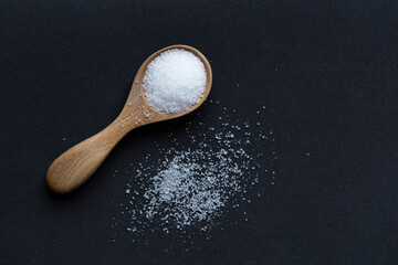 Salt in wooden spoon on black background