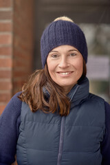 Attractive friendly smiling woman in blue winter outfit with knitted beanie hat and warm jacket in a close up head and shoulders outdoor portrait