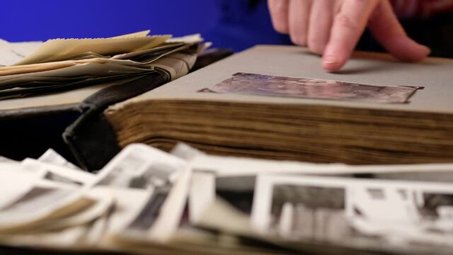 Elderly woman looks through an family album with old photos at table at home. Old granny memories past times and remembering his life.