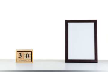 Wooden calendar 30 february with frame for photo on white table and background