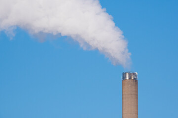 A closeup of an industrial smoke pipe against clear blue sky.