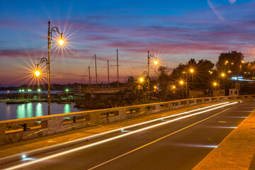Colorful sunset and light trails motion of the passing by cars. Long exposure view of a harbour, near at the entrance of the UNESCO – protected ancient town of Nessebar, Bulgaria. Tourism concept.