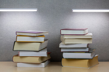 Several books lie on top of each other on a wooden table under two table lamps.
