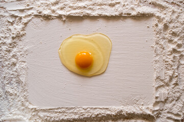 Flour sprinkled on a wooden table, with a smooth rectangular print and a raw egg in the center. Copy space. 