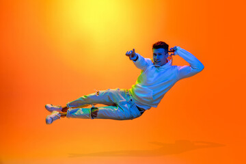 Fototapeta na wymiar Levitating. Caucasian man's portrait isolated on yellow studio background in mixed neon light. Handsome male model. Concept of human emotions, facial expression, sales, ad, fashion. Copyspace.