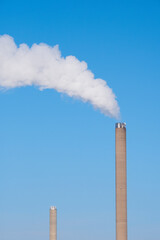 A closeup of an industrial smoke pipe against clear blue sky.