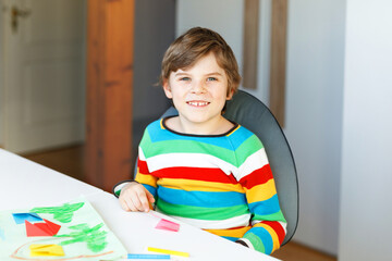 Little kid boy making paper origami tulip flowers for a postcard for mother's day or birthday. Cute child of elementary class school doing handicraft