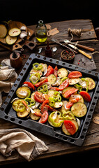 tasty slices of raw veggies (eggplants, tomatoes, pepper, onion, herbs) on baking tray on rustic wooden table