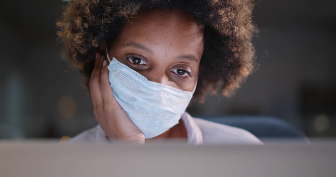 Young african businesswoman in protective mask looking at laptop display working with data in office