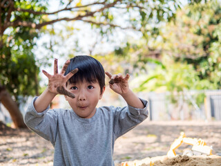 Asian cute child boy showing dirty black hands with clay, soil with wow funny face while playing outdoor. Happy kid enjoy in relaxing day, preschool learning and freedom concept.