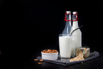 glass and bottles of vegetarian oatmeal and almond milk on dark background