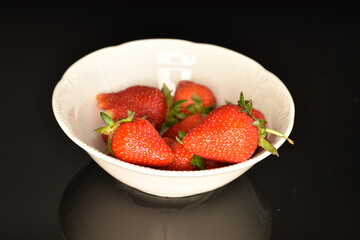 Several organic strawberries in a white ceramic plate, on a black background.