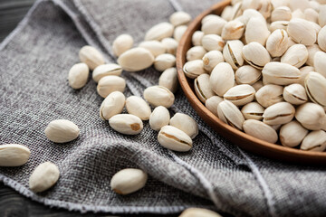 Wooden bowl with nut pistachios.  on a wooden background, near a bag from burlap. Healthy food and snack, organic vegetarian food. (selective focus; close-up shot)
